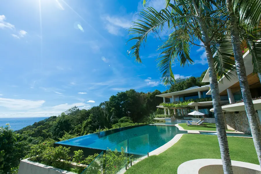 Infinity pool and lawn under palm trees with the sea beyond